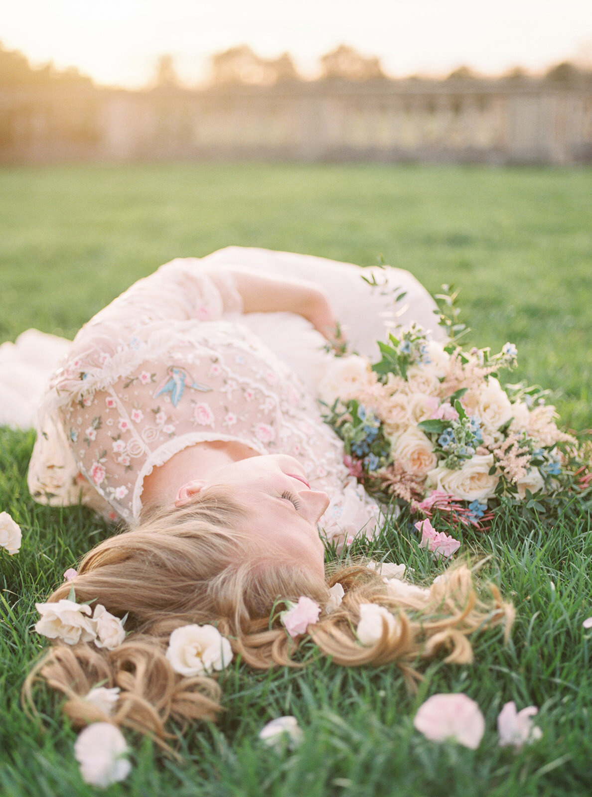 Blonde mother lays in grass with flowers in her hair.
