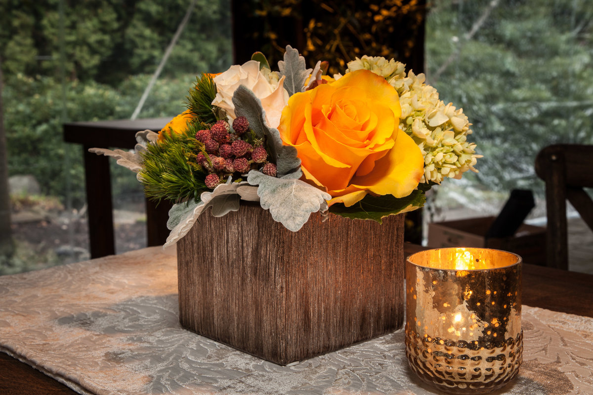 centerpiece of orange rose, dusty miller, in square vase and gold votive