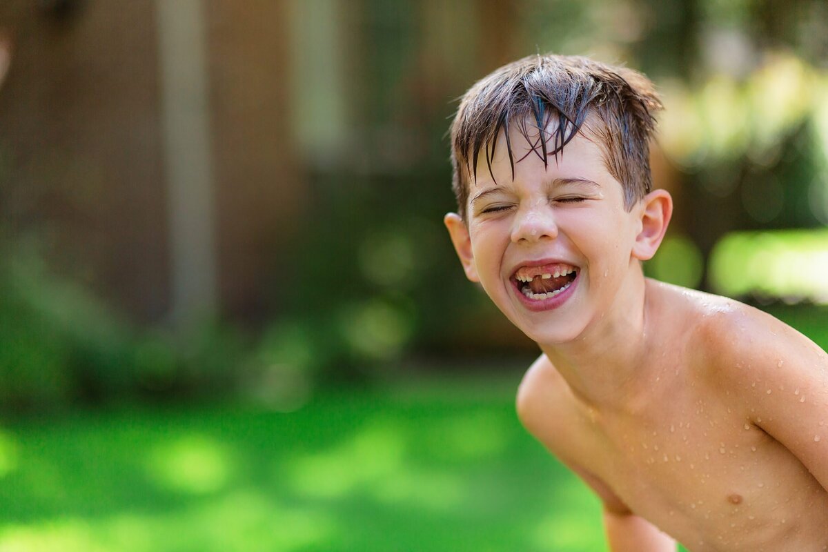 A young boy plays in his front yard and smiles.