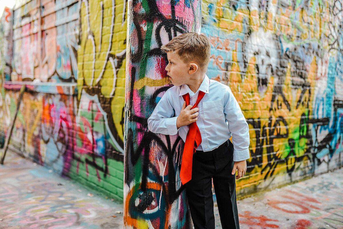 Little boy wearing a white shirt and pulling off a red tie in graffiti alley near MICA in Baltimore Maryland