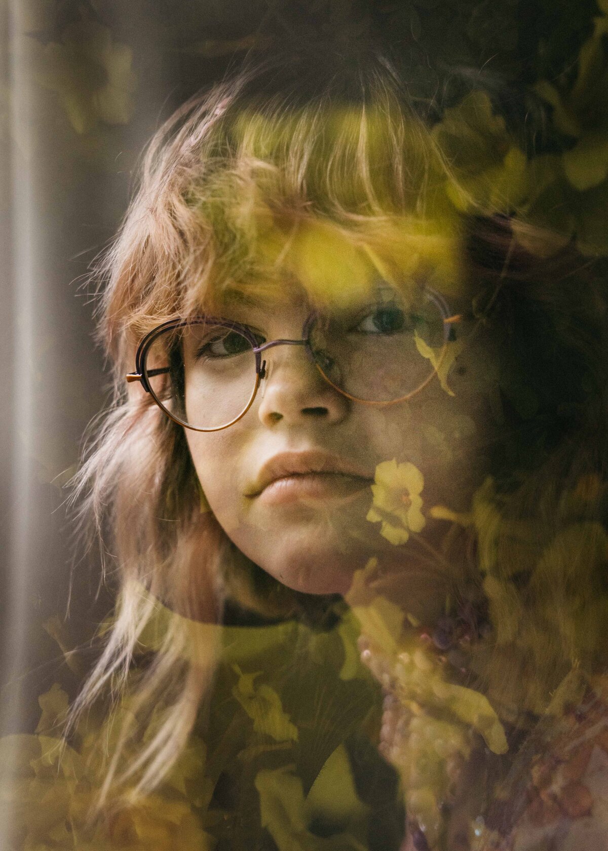 Teenage child with pink hair is looking out a window. 