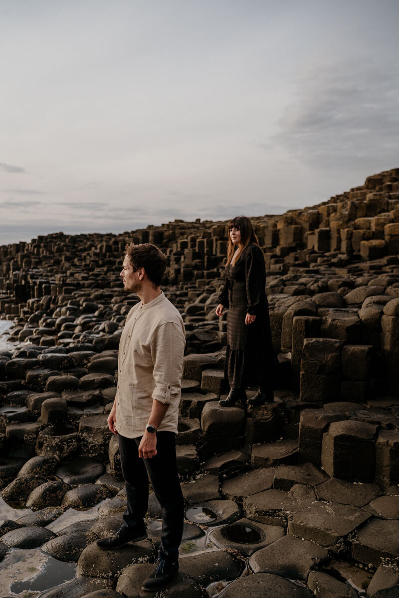 Séance photo de couple en irlande, sur les roches noires de la Chaussée des Géants avec un couple face à l'océan.