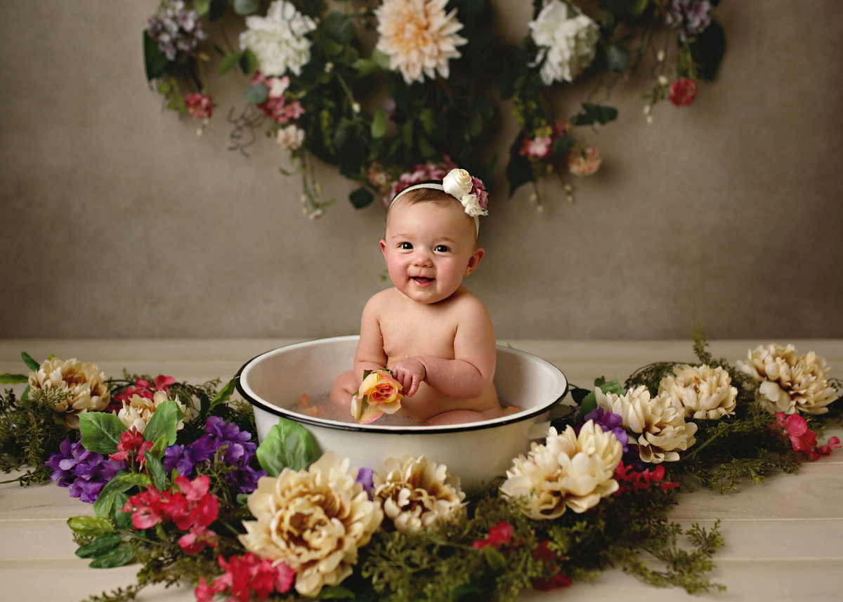 baby girl in farmhouse metal wash bin surrounded by flowers