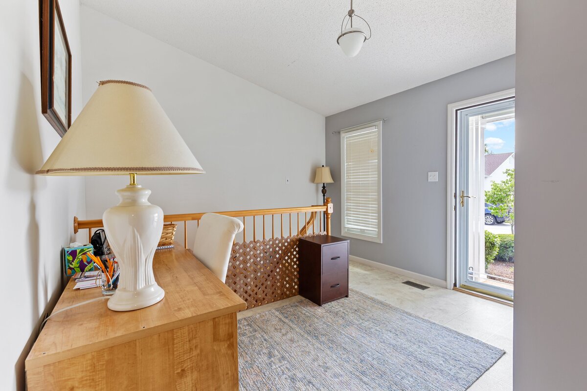 Listing photo for real estate showing the entrance of a house, with the front door and a window to the right. Stairs and a desk are to the left of the photo.