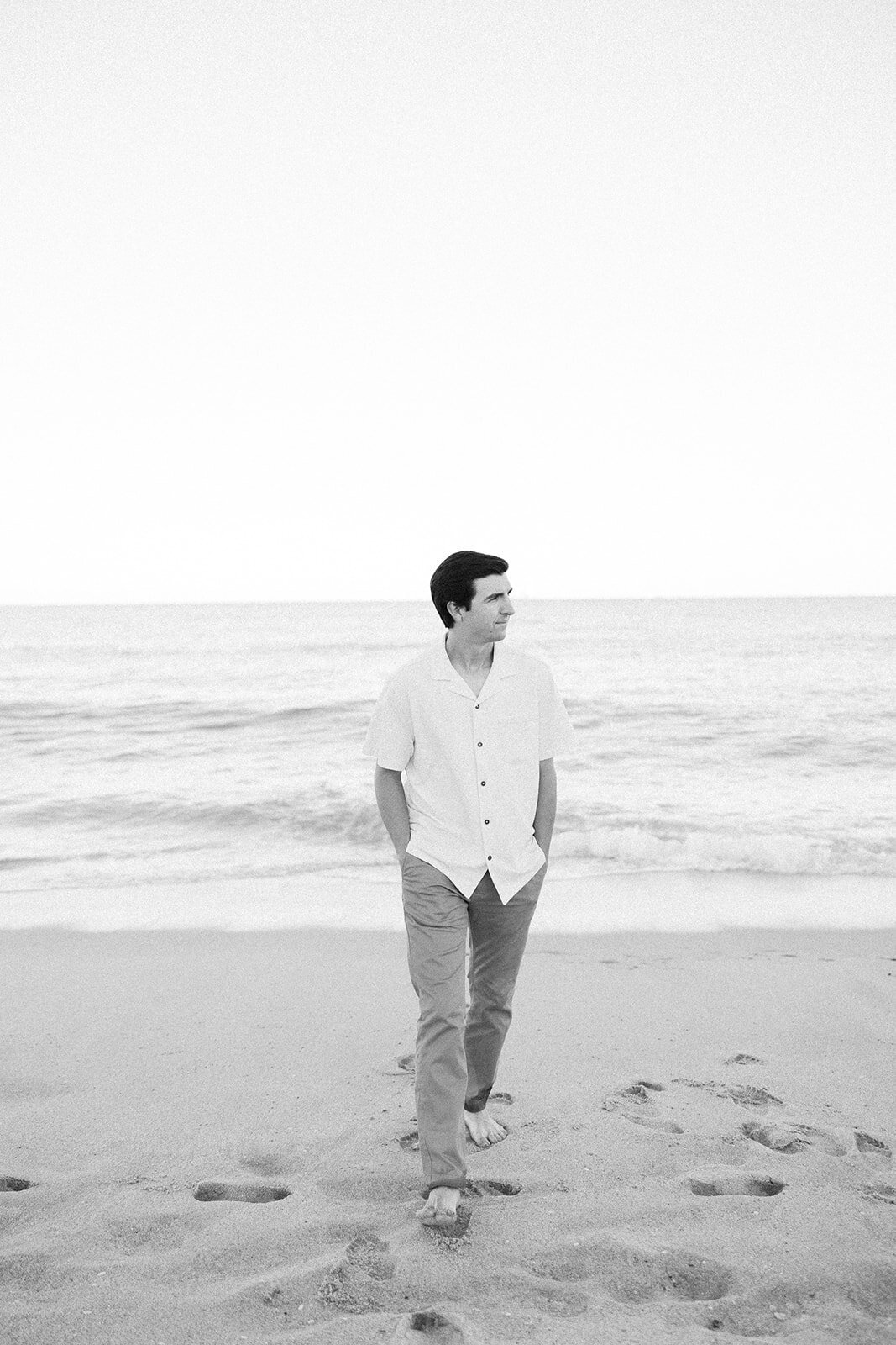 Graysen walks along the sandy beach, enjoying the ocean breeze during his Florida engagement session at Marriott Hotel Fort Lauderdale, beautifully documented by Claudia Amalia.