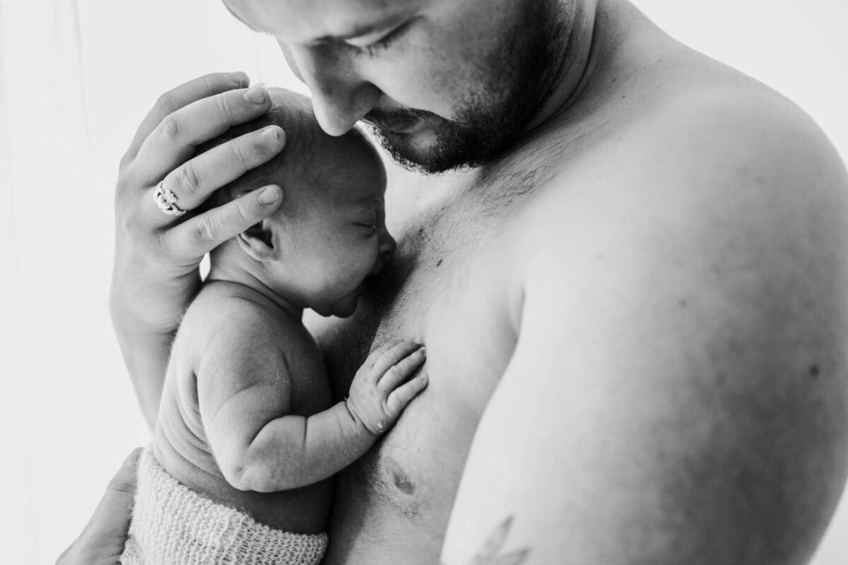 Ruua Hamdan Photography (UK): A black and white image of a dad holding his newborn baby close to his chest.