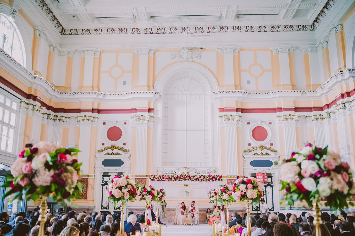 An indian couple performing rituals during their hindu ceremony under the mandap inside the please touch museum in philadelphia