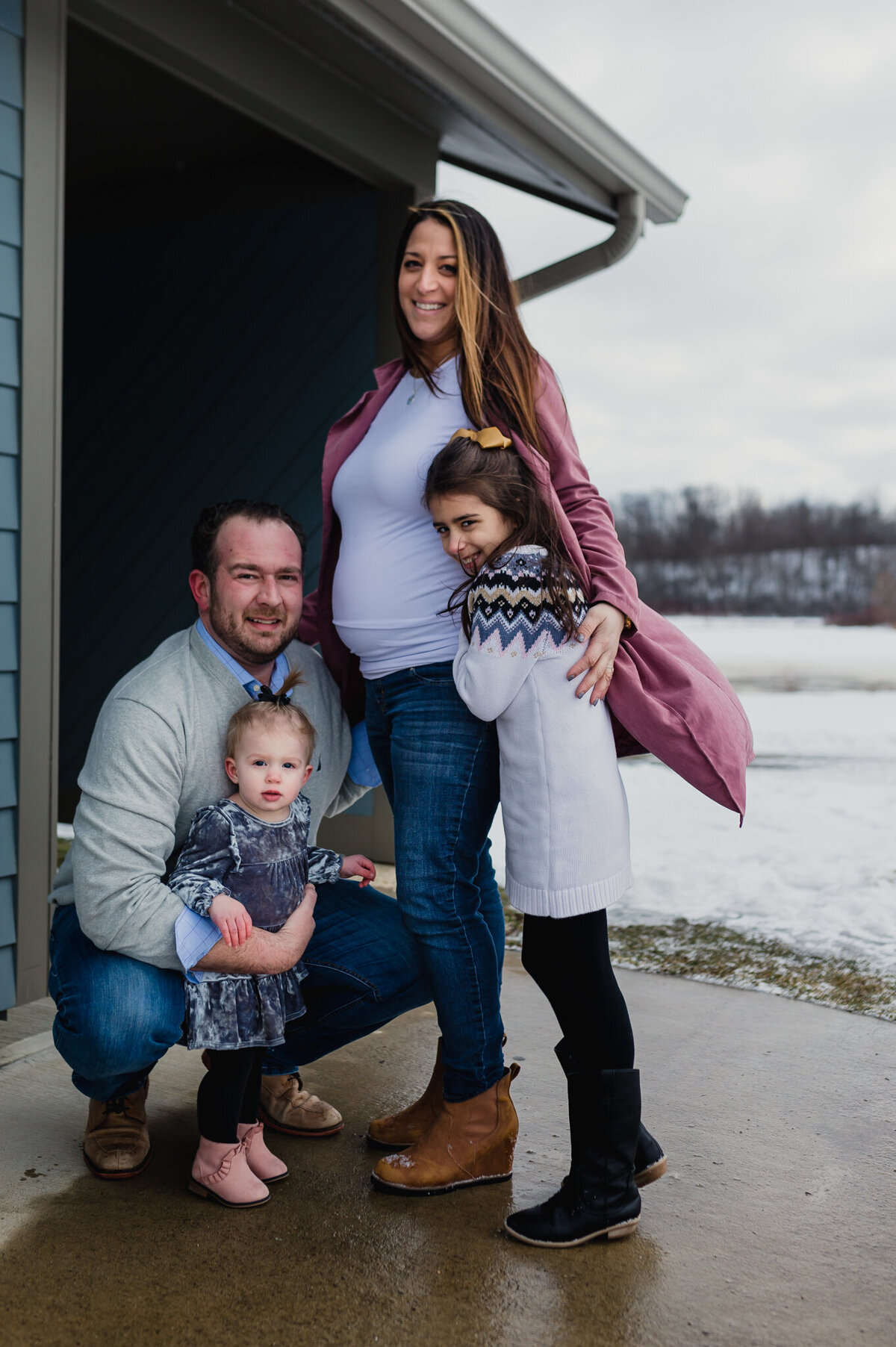 A family photoshoot with mom, dad, and two daughters smiling at camera.