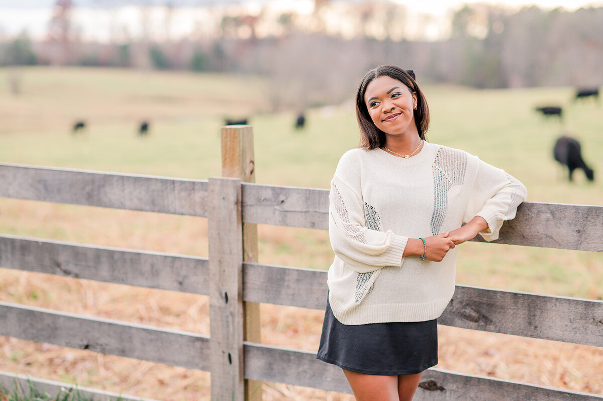 girl posing next to a wooden fence with cows in the background