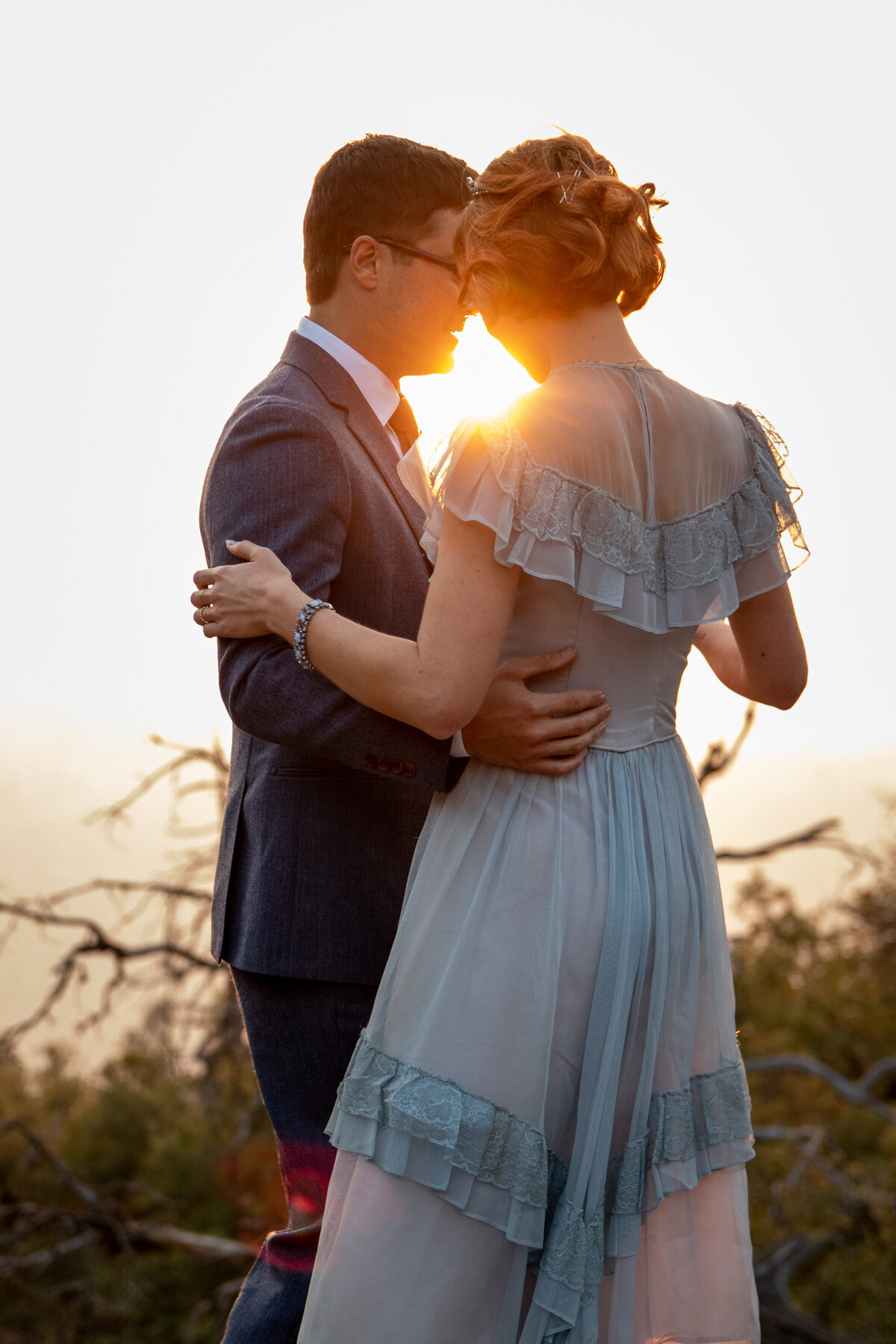 A bride and groom stand close to each other dancing on their Yosemite elopement day as the sun shines through between their heads.