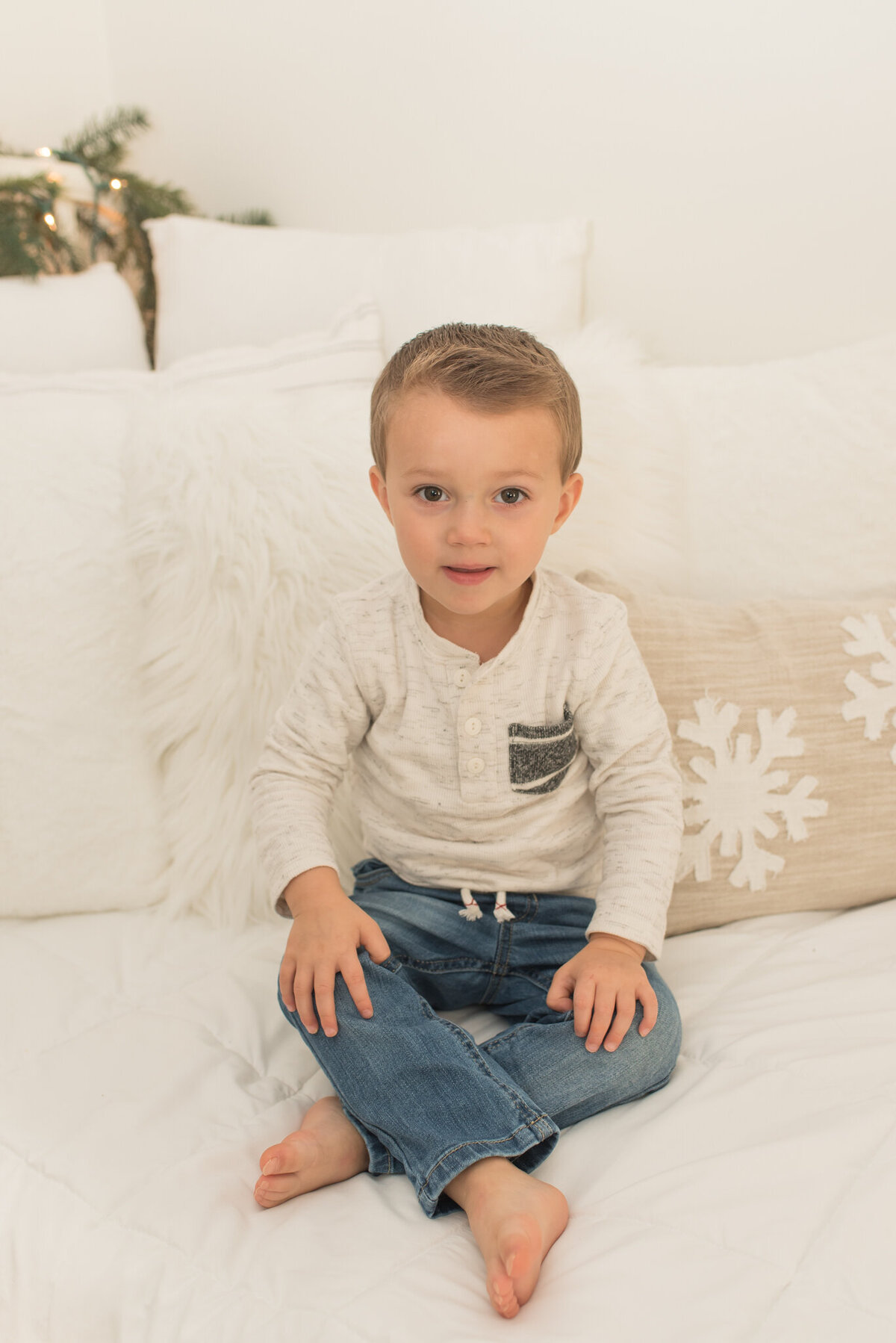 Young boy wearing tan sweater sitting on white bed