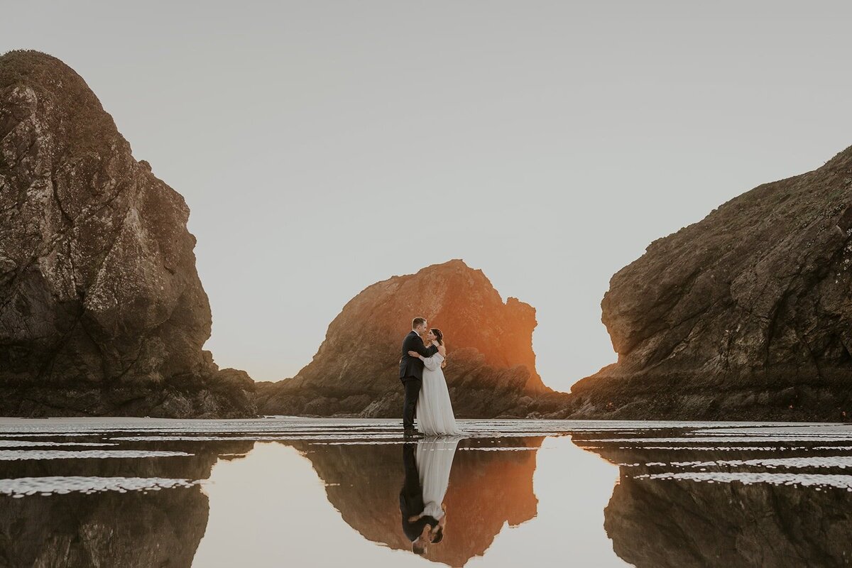 An eloping couple stands on the beach in wedding attire on the Oregon Coast