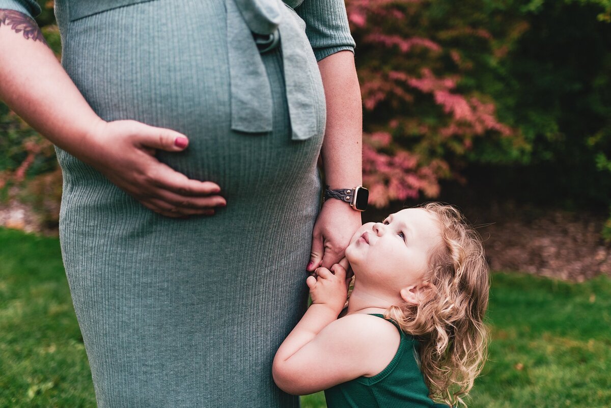 sibling looking at pregnant Mom. Holding hands and cuddling.
