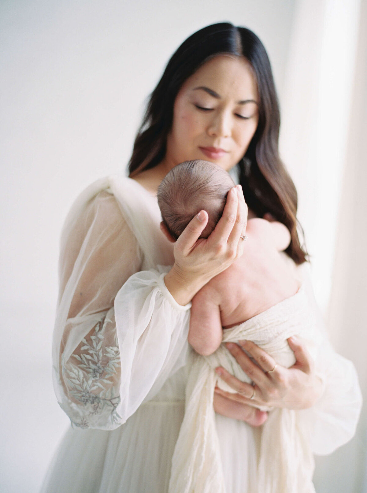 Mother holding newborn against neutral backdrop, Bay Area newborn photographer session.