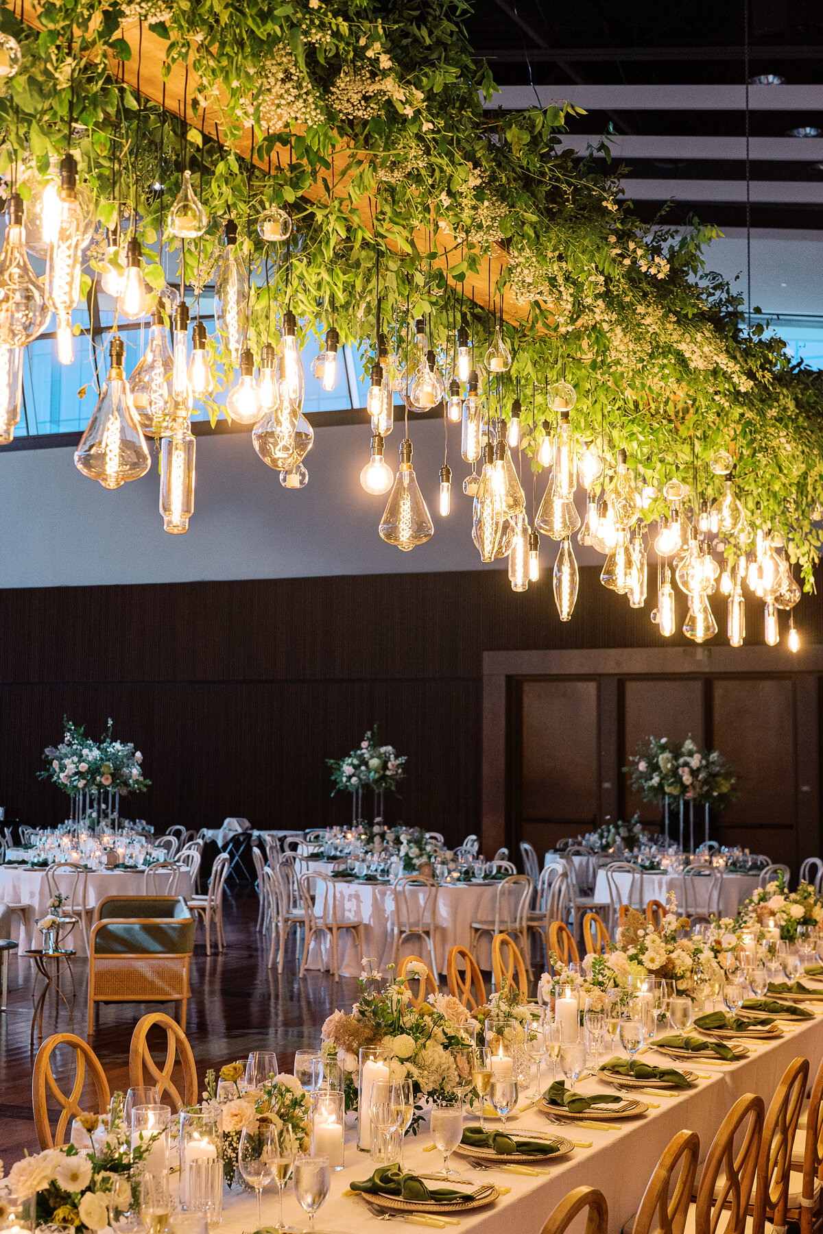 Epic floral installation for garden-inspired summer wedding. Large and lush floral install over head table for timeless wedding design. Vine-like greenery and florals accent this hanging Edison bulb installation. Downtown classic white and green wedding. Design by Rosemary & Finch Floral Design in Nashville, TN.