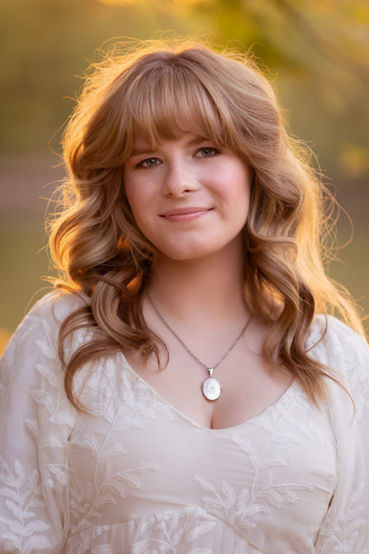 Dallas senior photographer captures a close-up of a young woman with soft waves in her hair and a silver necklace, glowing in the warm sunset light.