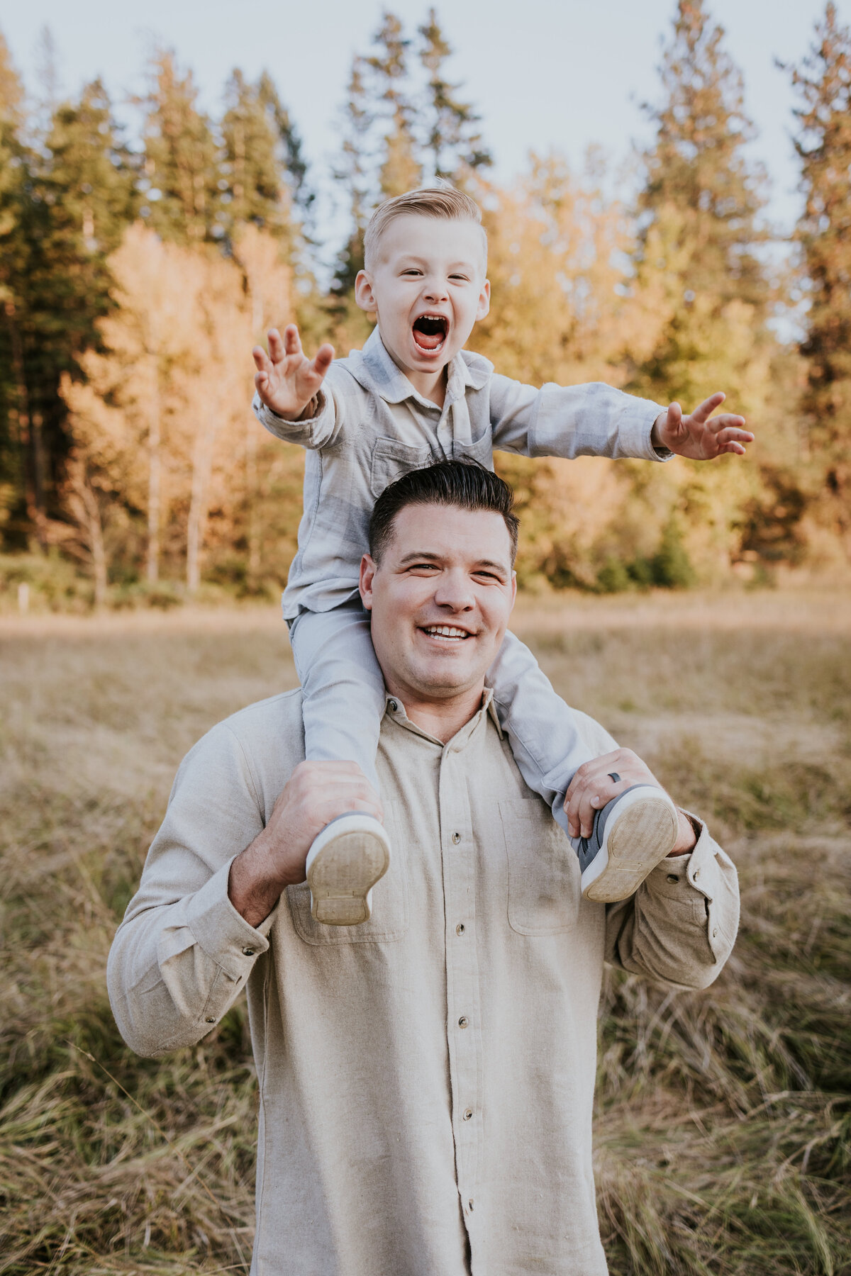 Dad holds young son on shoulders while both give the camera huge smiles.