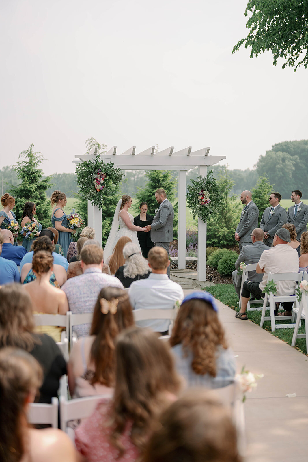 Full ceremony view showing guests, floral arrangements and the rustic outdoor setting at The Blue Heron Barn wedding venue.