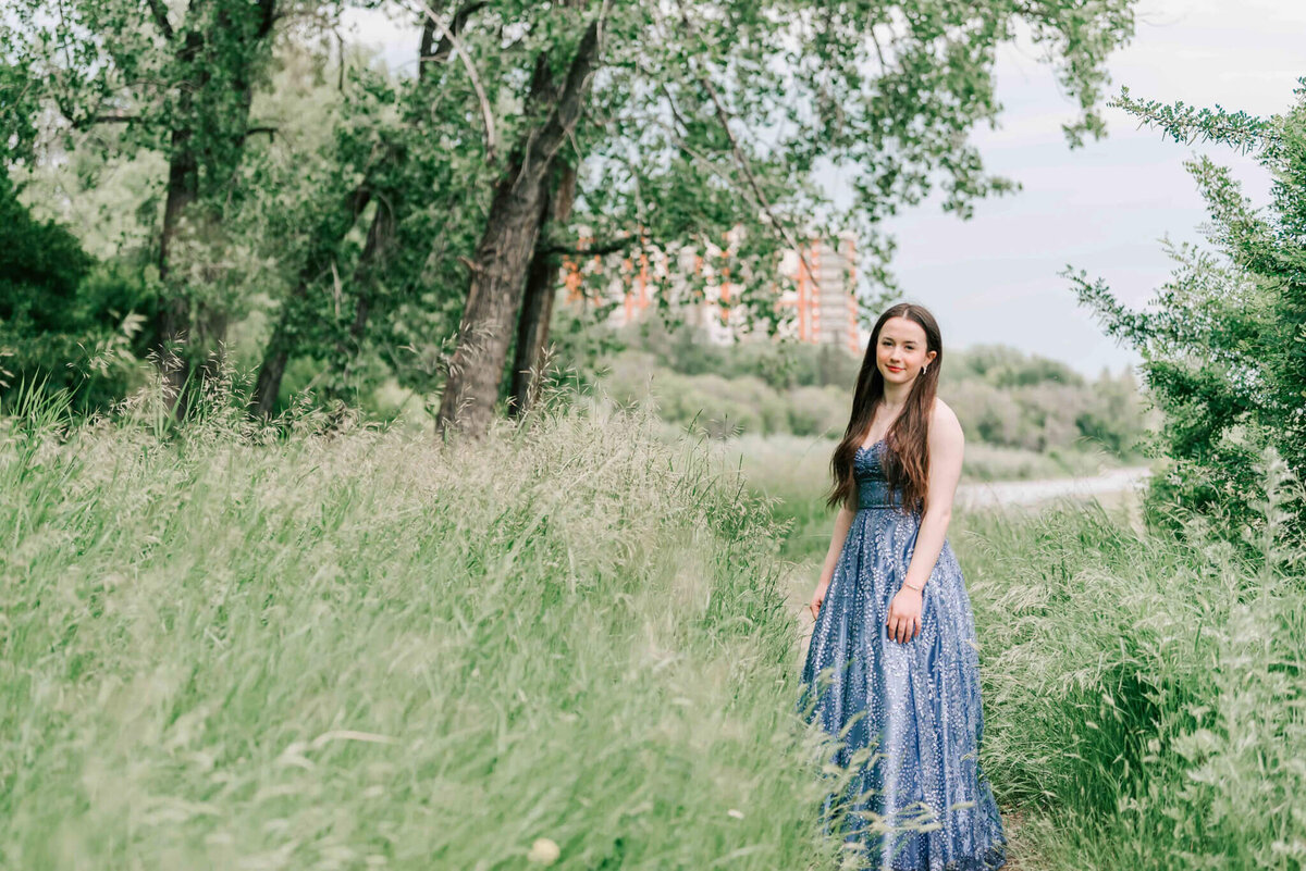 A girl with dark hair standing on a dirt path by trees. 