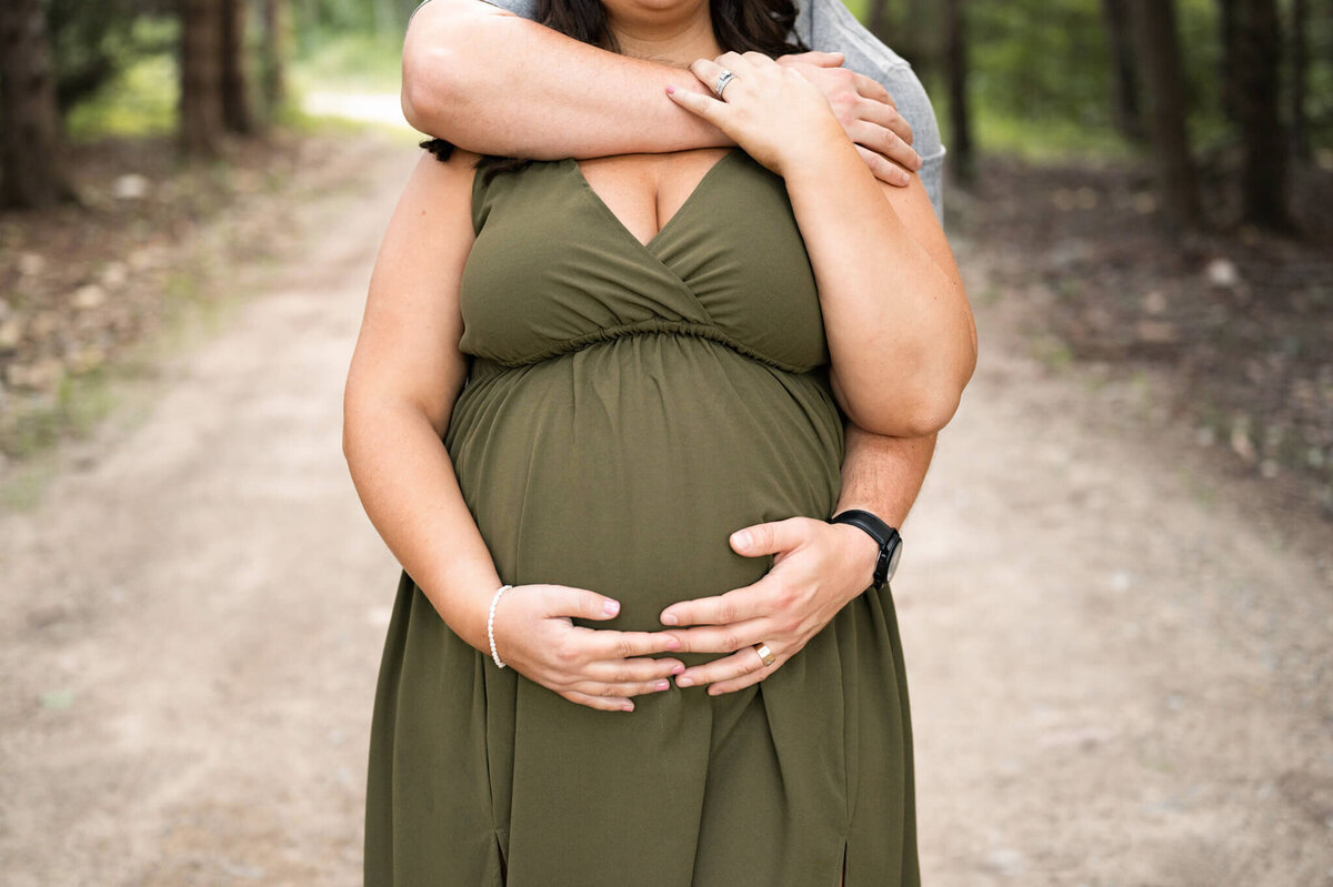 Up close shot of pregnant belly while husband hugs wife standing behind her
