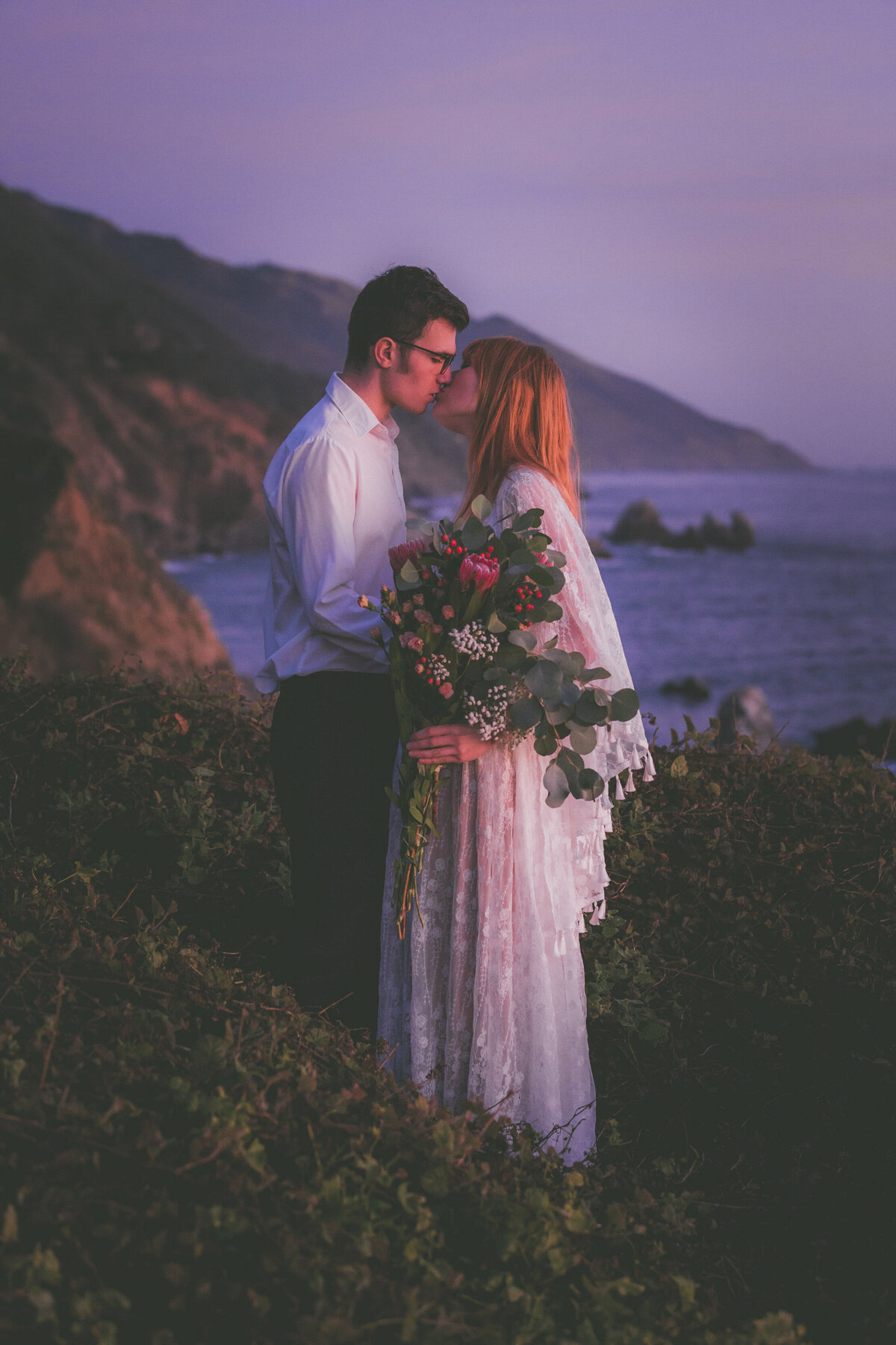 Bride and groom kiss with Big Sur scenery.