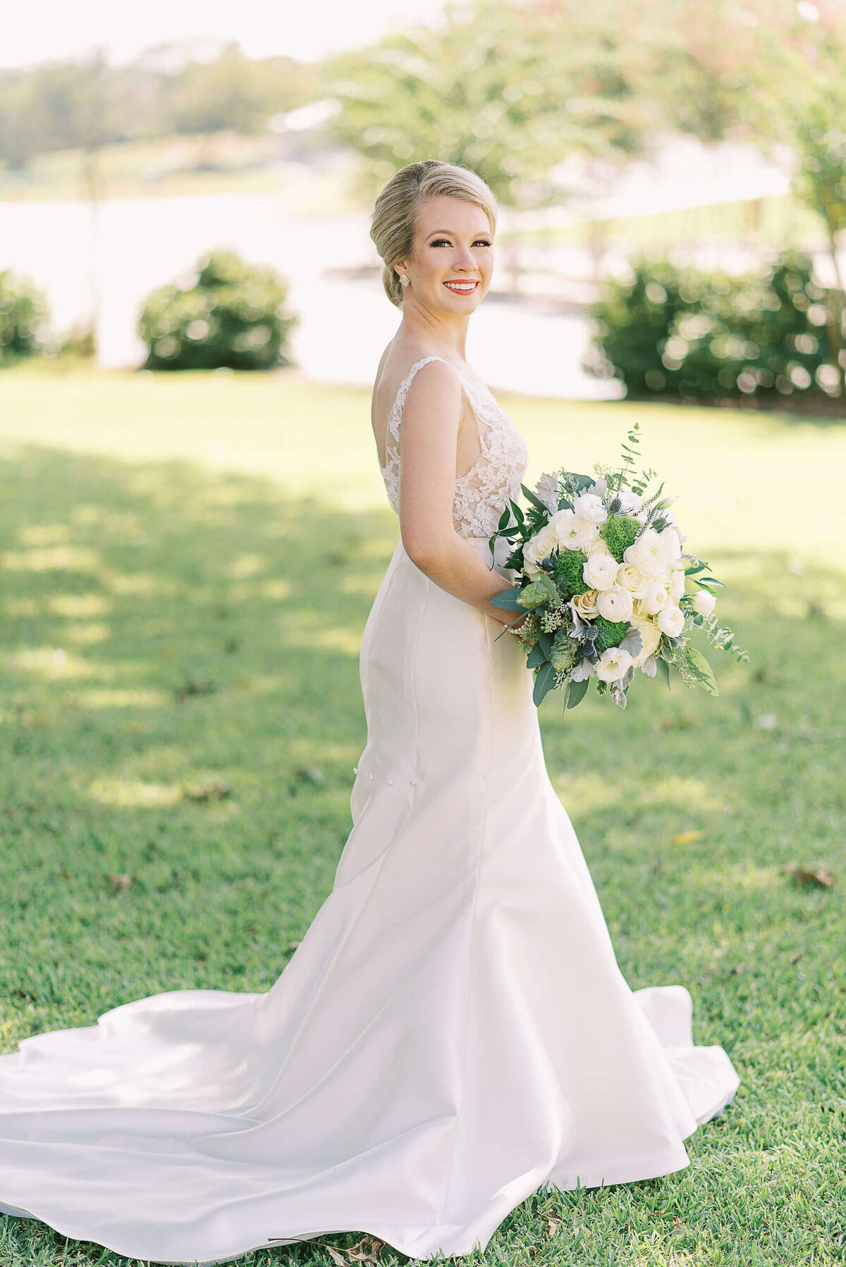 Happy bride with blonde hair holds bouquet and poses in her white wedding dress