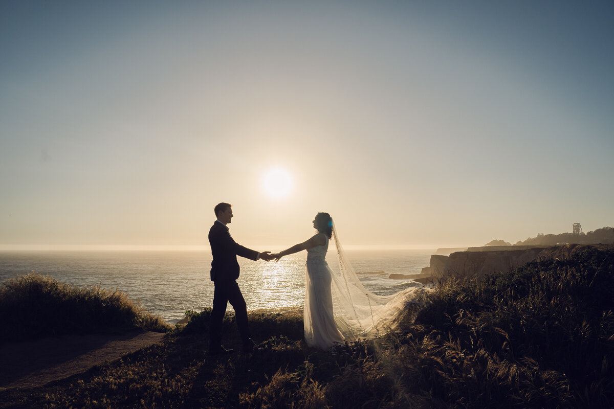 Bride and groom at Shark Fin cliff during sunsets while they hold hands lovingly