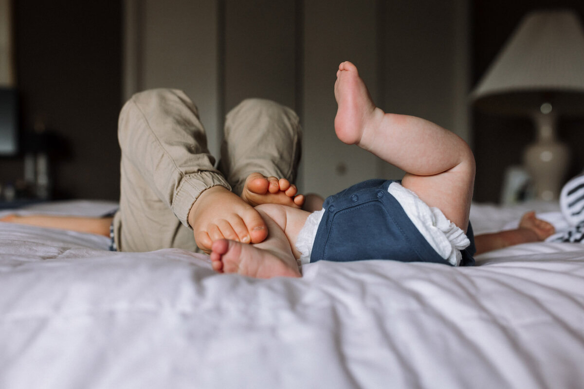feet of toddler and newborn laying on a white comforter in parents' bed
