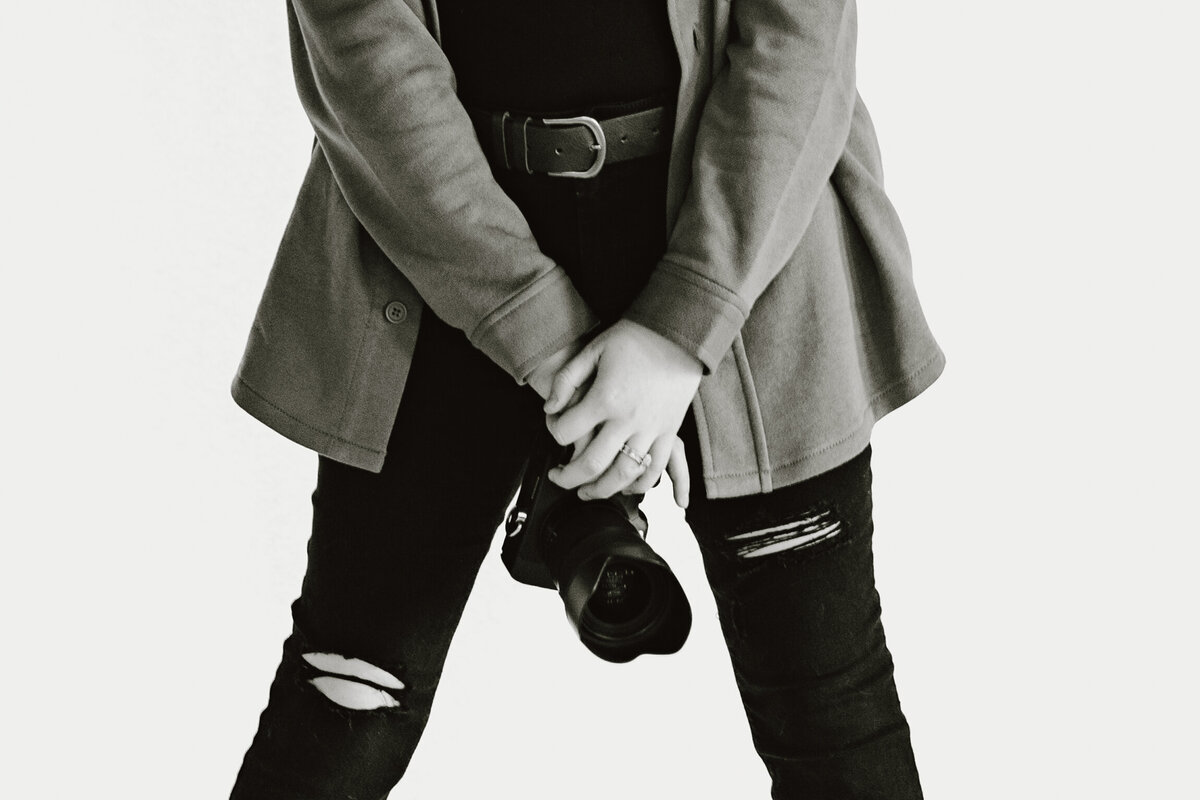 Contact form headshot photo of the photographer, photographer is posing in studio holding up their camera like they are going to take a photo