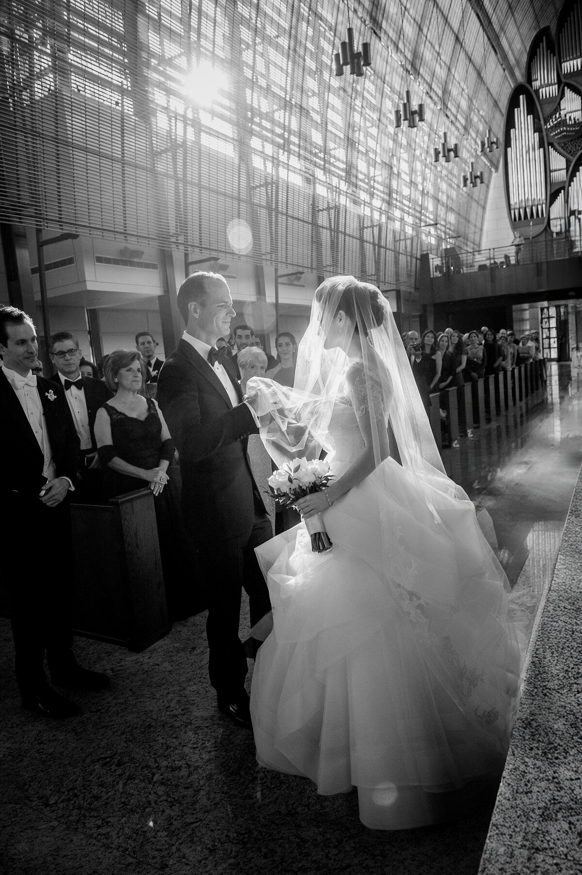 A groom lifts his bride’s veil during a heartfelt church ceremony, surrounded by loved ones, captured by Rodrigo Varela Photography.