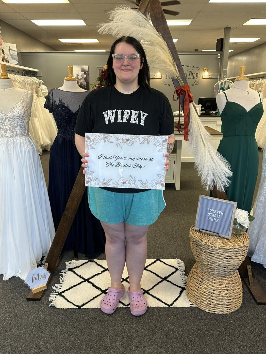 Woman wearing a ‘Wifey’ shirt holding a sign inside a bridal shop