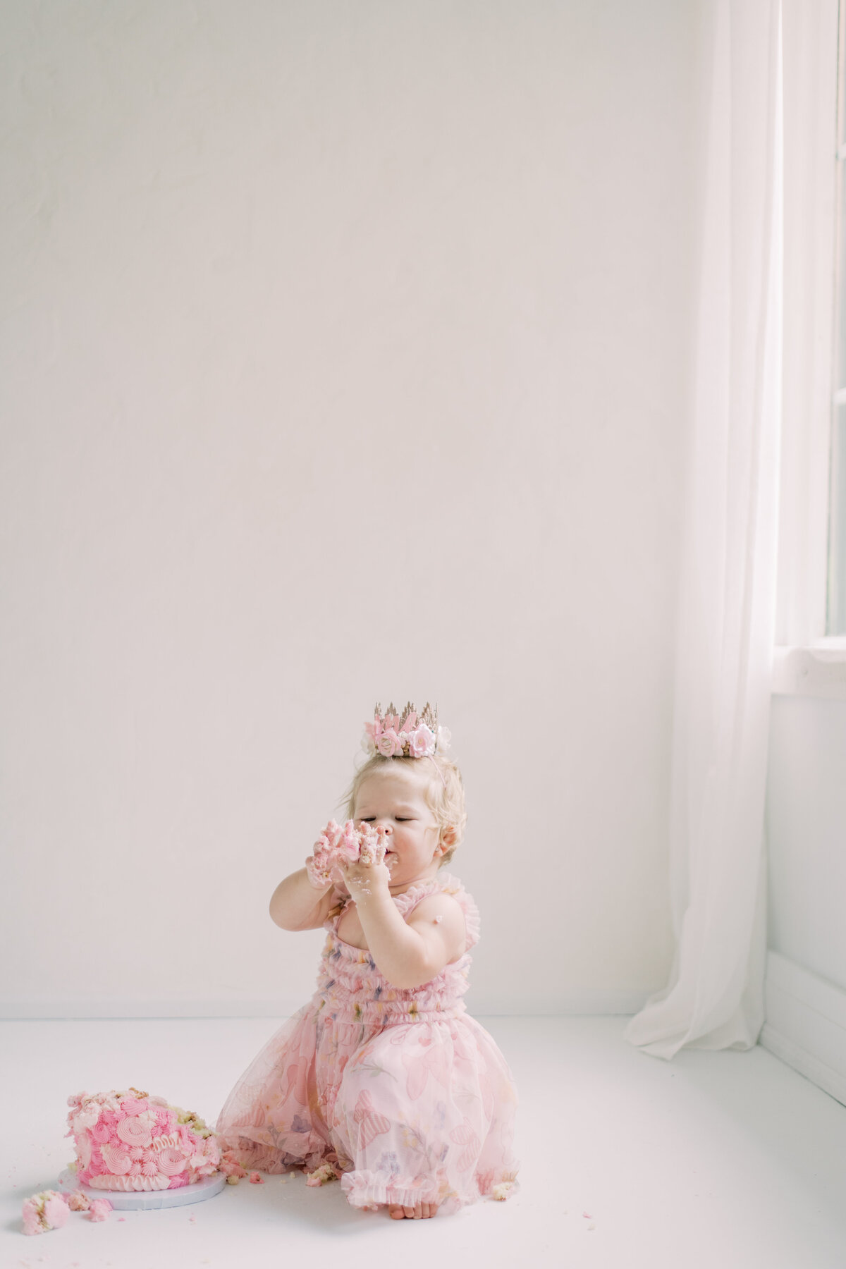 Adorable baby girl in soft pink dress and crown during elegant cake smash session