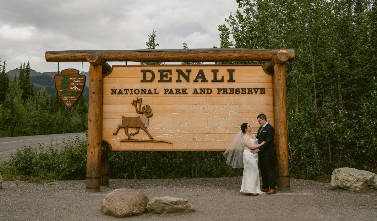 a bride and groom by the Denali Park sign in Alaska