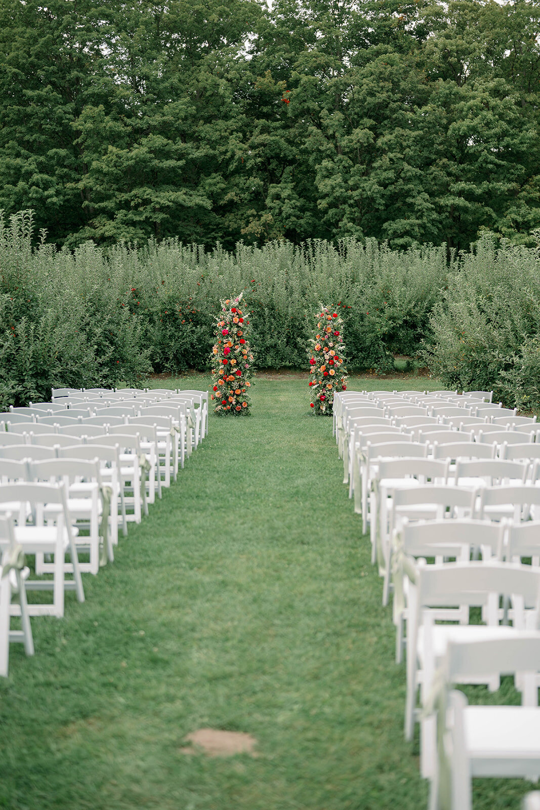 The ceremony space with empty chairs and vibrant floral arch set up in the apple orchard at The Cherry Barn, a fall Michigan outdoor wedding venue.
