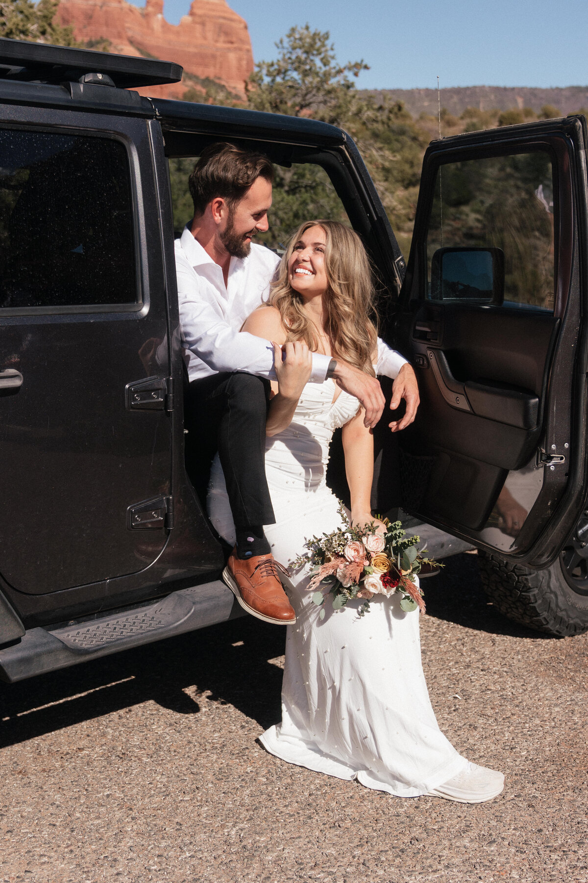 A happy couple sharing a joyful moment in a Jeep during their Sedona elopement at Merry Go Round Rock, dressed in white with sunshine highlighting their smiles.