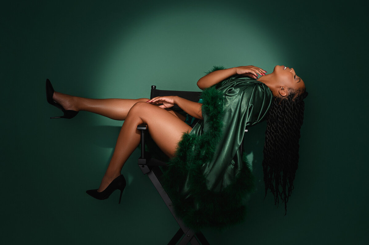 Model in a green satin robe, reclining in a director's chair with dramatic lighting and high heels