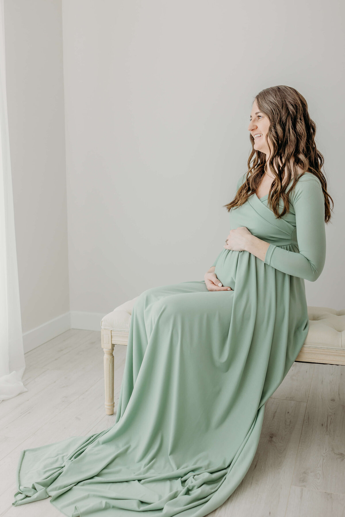 Mom laughing and looking out window pregnant in long green dress sitting on bench
