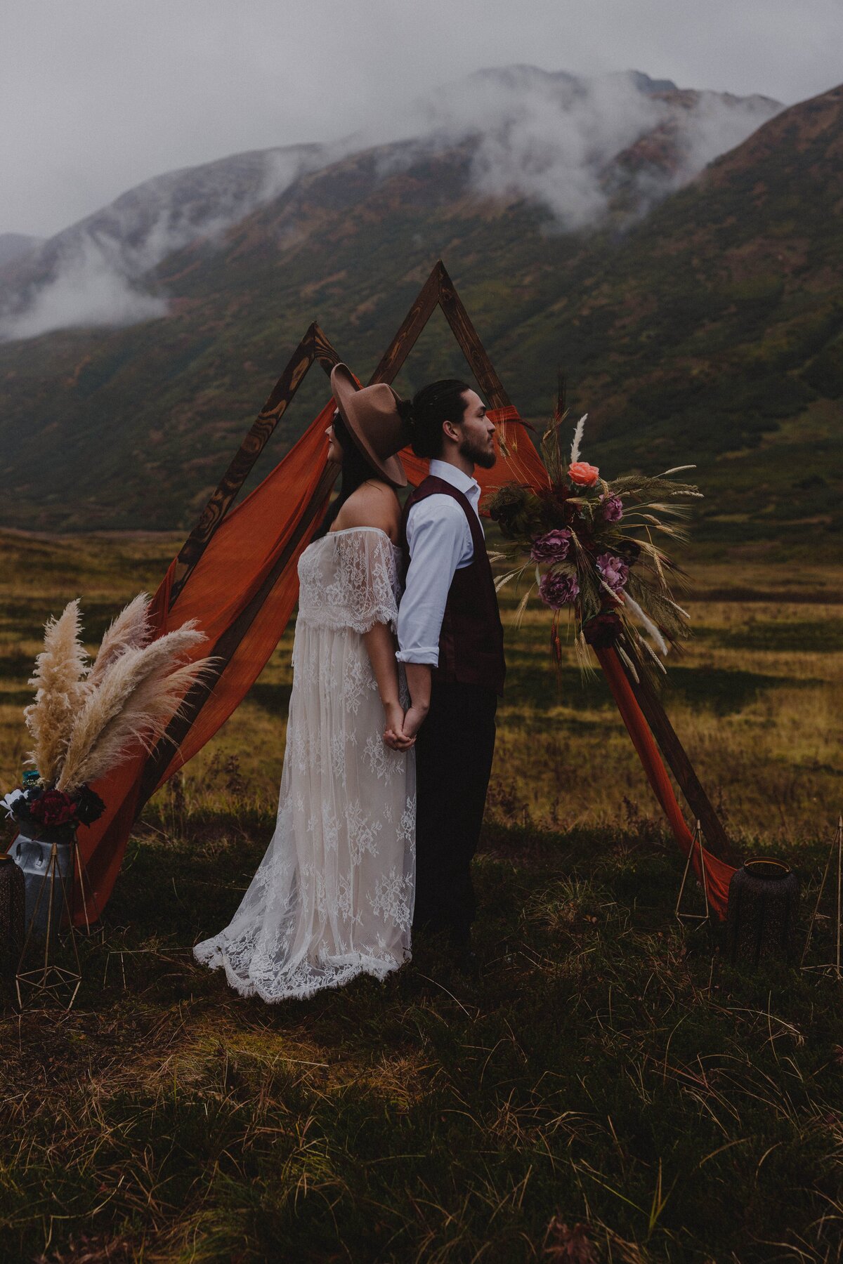 A couple poses in front of their wedding arch in Turnagain Pass, Alaska