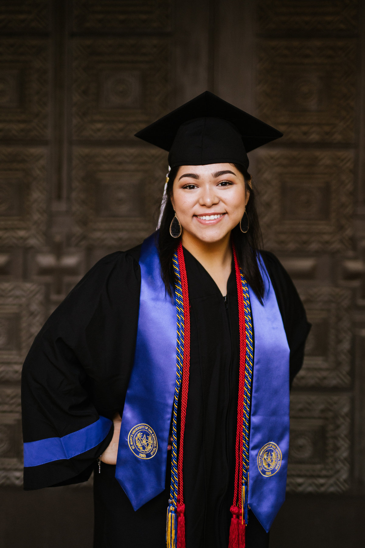 college in senior cap and gown with cords in doorway