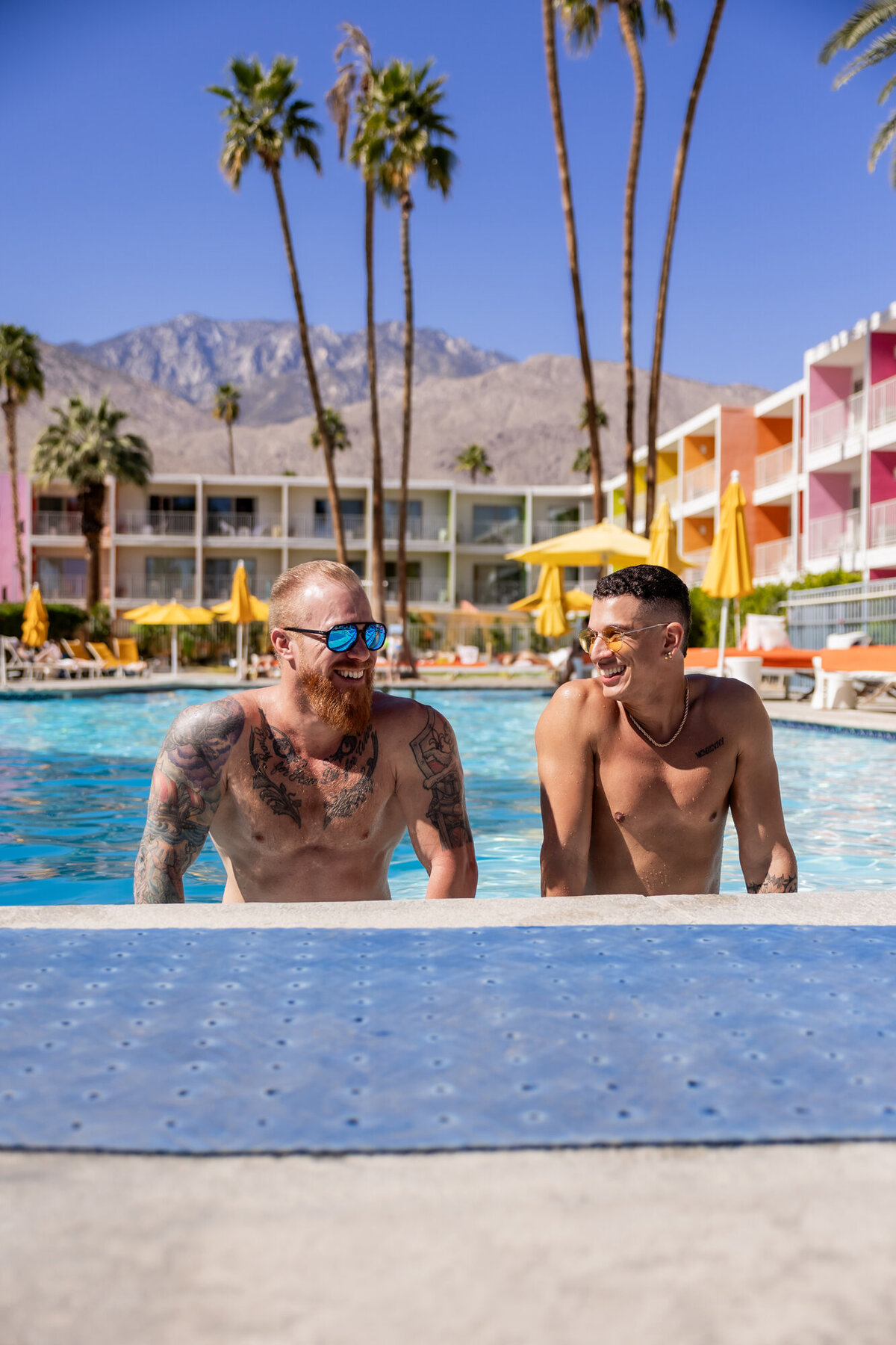 Two models posed side-by-side in the pool, framed by mid-century design and vibrant resort tones.