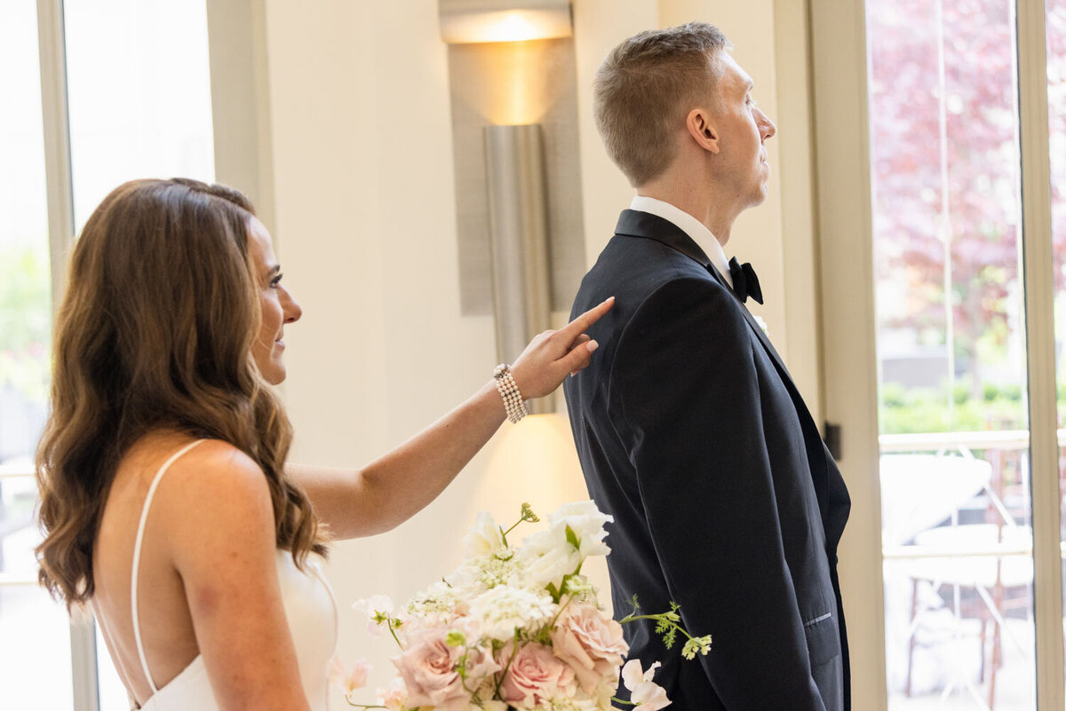 A bride and groom are getting ready for their wedding and the bride is pointing at the groom 's back.