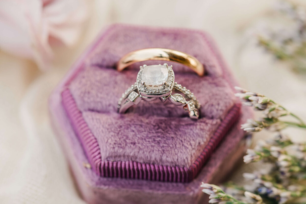 Close up of sapphire and gold wedding rings in a purple box accompanied with wedding florals