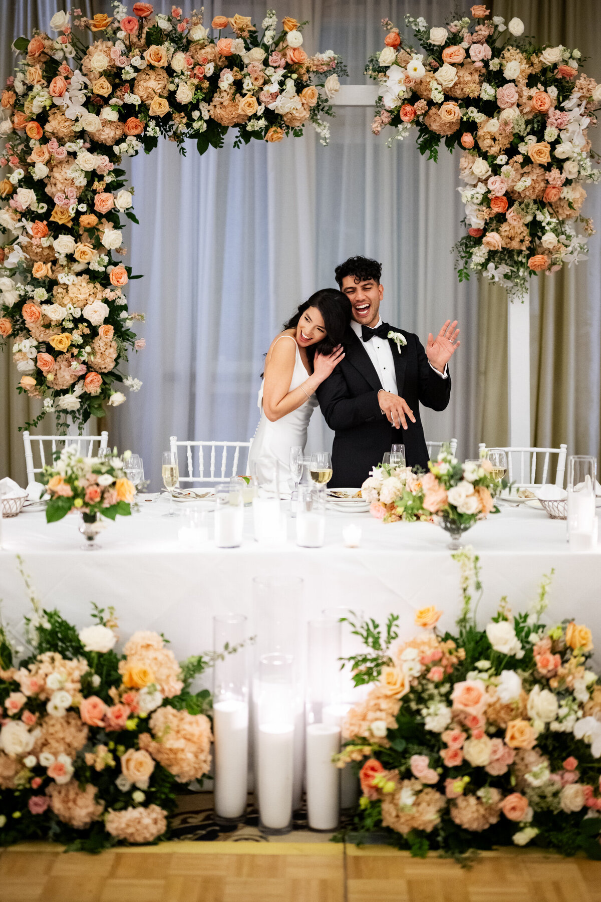 San Francisco Bay Area wedding photographer documents authentic celebration moment as bride and groom embrace under elaborate floral arch at Santa Monica wedding