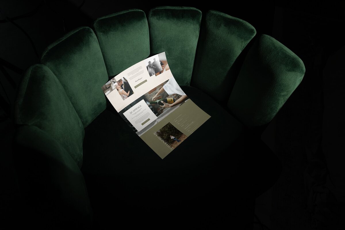 An open brochure with images and text lies on a dark green, shell-shaped upholstered chair against a dark background, evoking the elegant style often found in premium Showit website templates.
