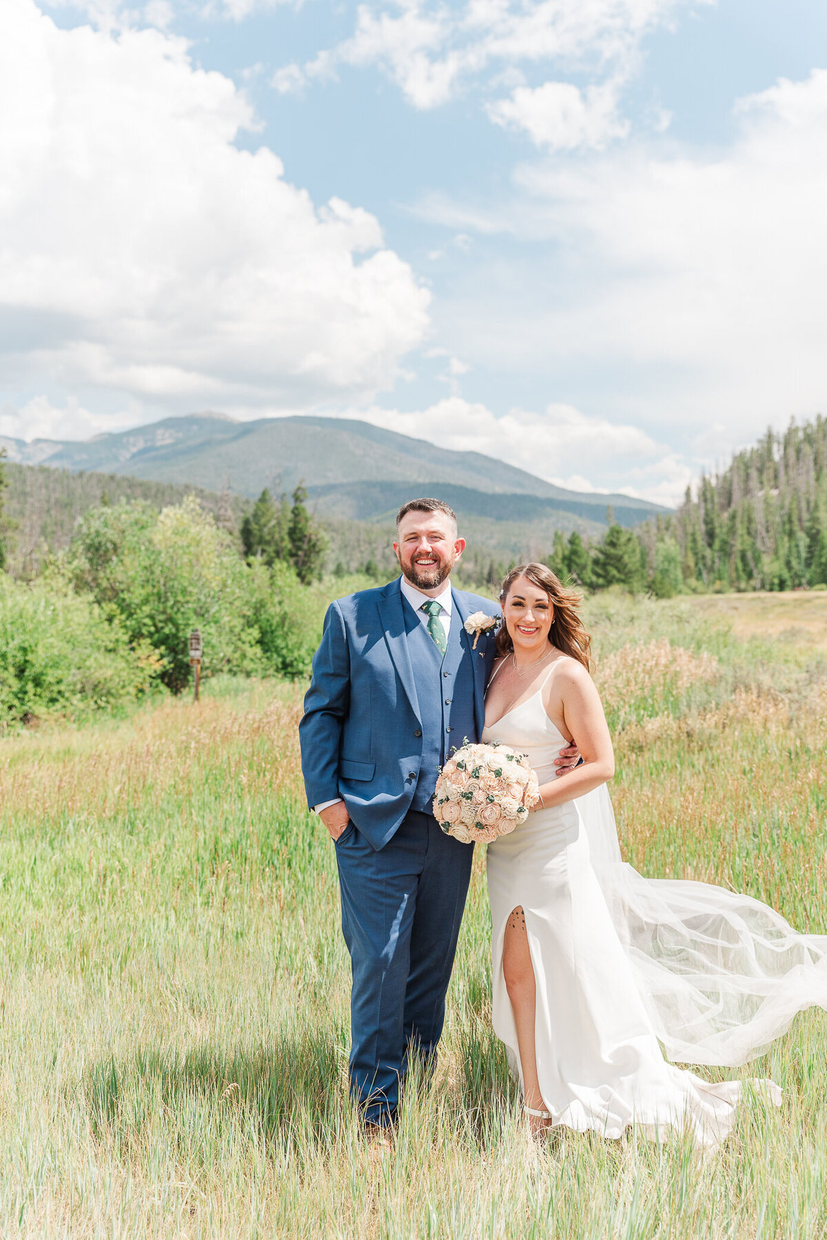 Bride and groom smile outside with mountains in the background captured by Denver wedding photographer