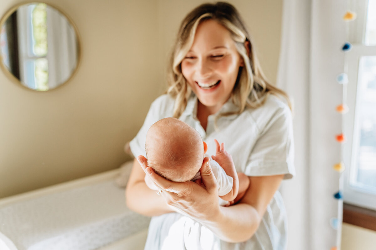 A bright, joyful moment of a mother holding her newborn baby, facing the child with a beaming smile.