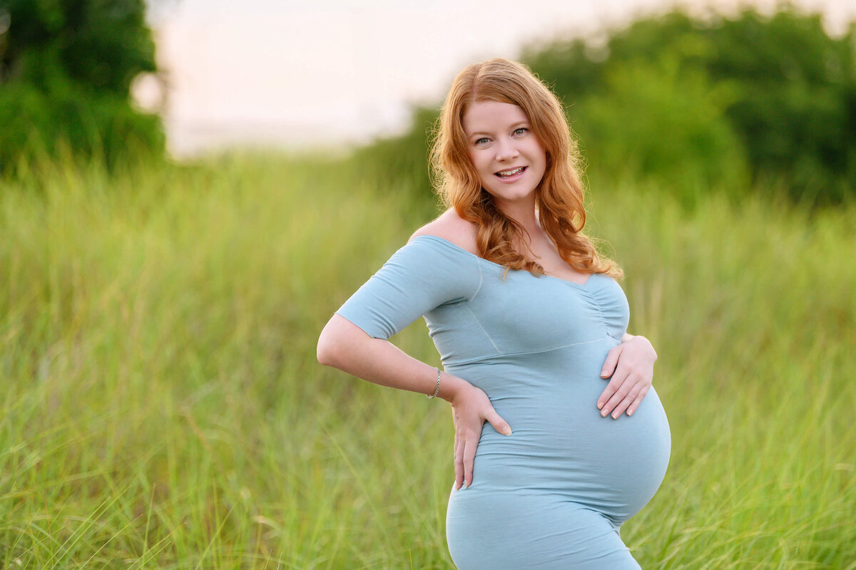 pregnant woman holding her belly wearing a blue dress with the sun setting behind for her Burlington, Ontario outdoor beach maternity photos