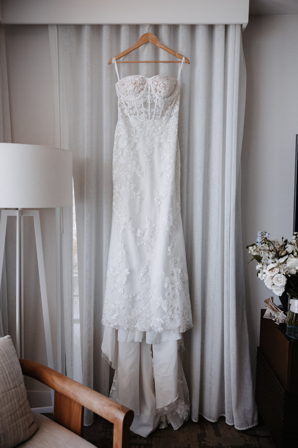 Vera Wang strapless lace wedding dress hanging in front of a curtain in hotel room