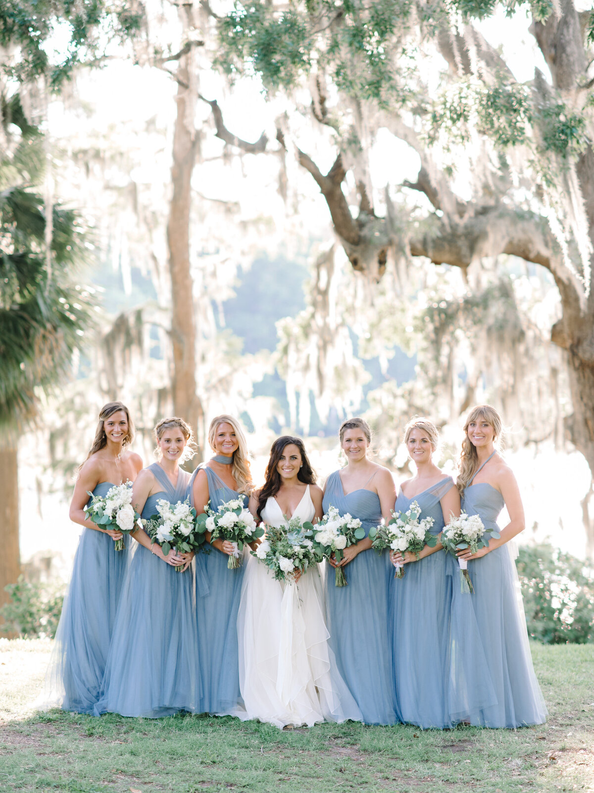 Joyful bridesmaids in light blue dresses raising bouquets with the bride
