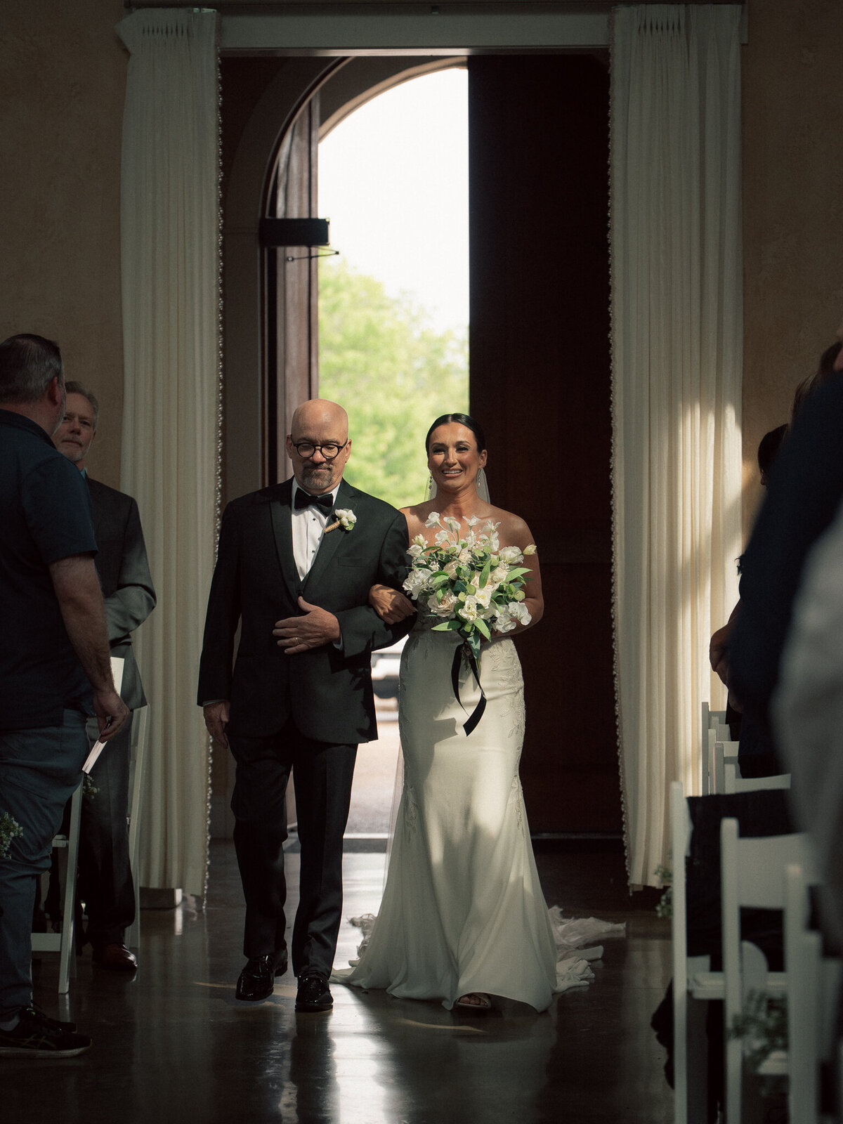 Bride walking down aisle with father during elegant indoor wedding ceremony